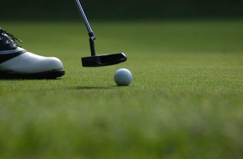 Up close shot of a putter about to hit a white golf ball on a green