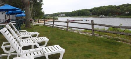 Three white lounging chairs on a green lawn overlooking an expansive river