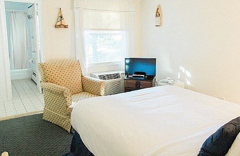 Bedroom with single bed, yellow chair, small TV and doorway into a bathroom