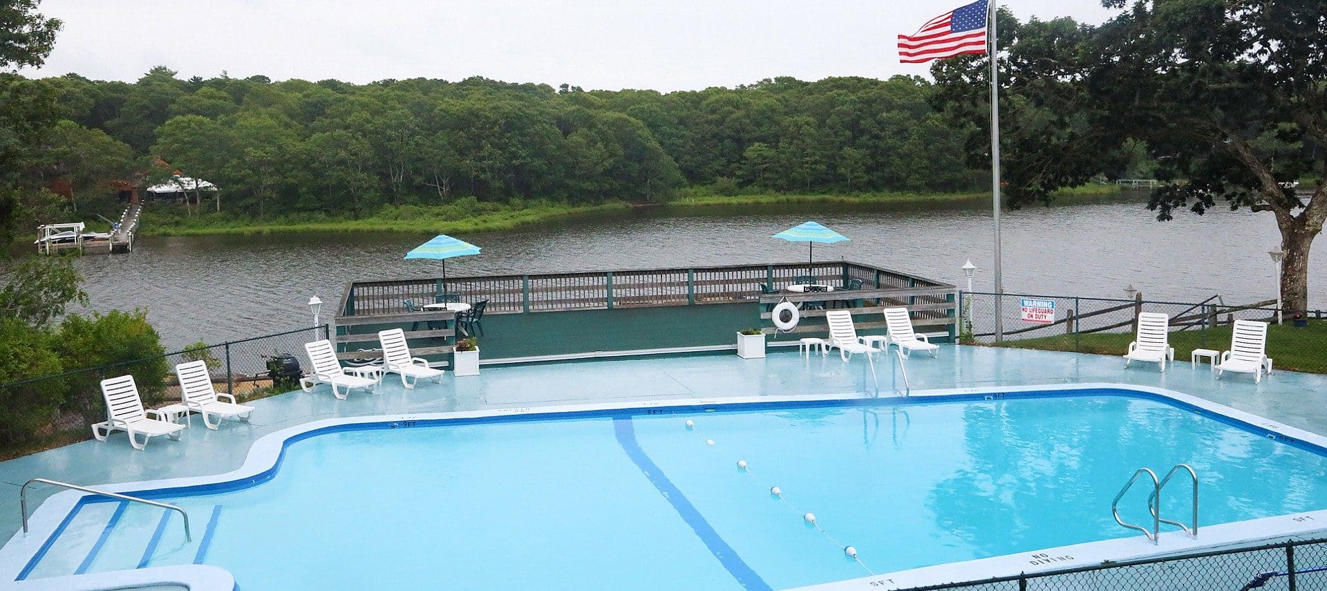 A large swimming pool with white lounging chairs and green deck overlooking a body of water