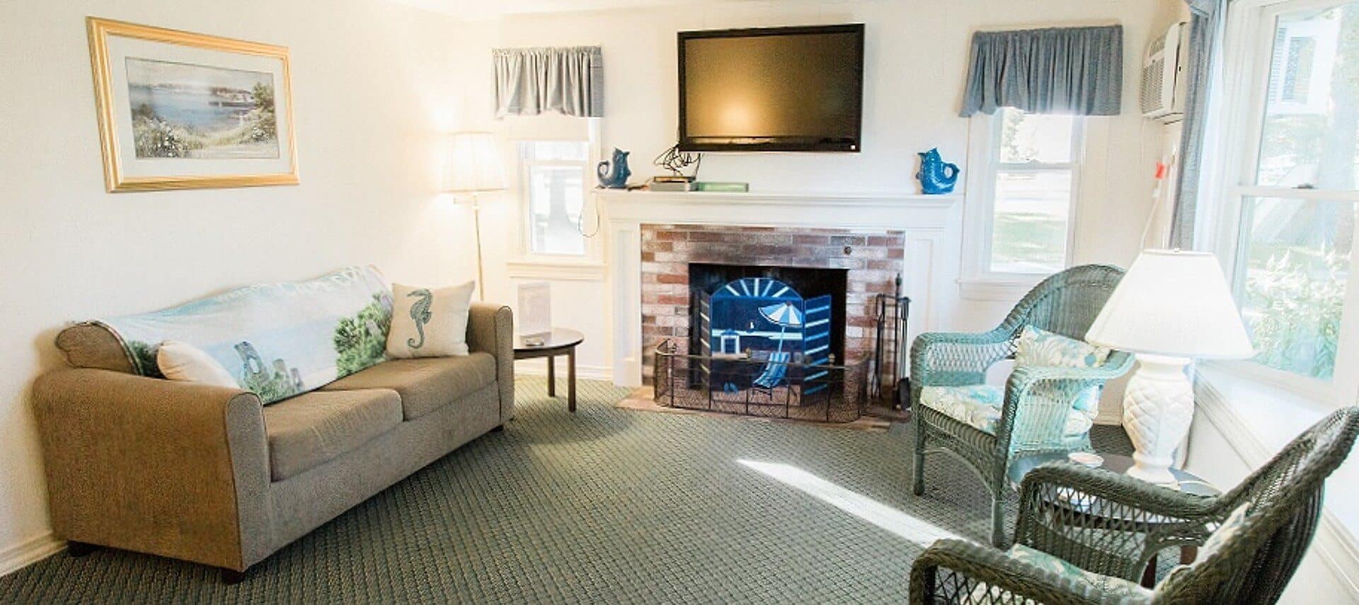 Living room of a cottage with fireplace, TV, couch and two green wicker chairs