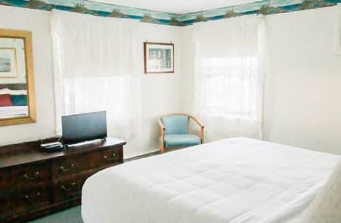 Guest room with queen bed, sitting chair and dresser with small TV