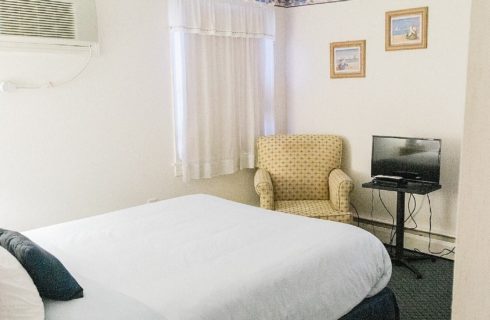 Bedroom with single bed, yellow upholstered sitting chair and small TV