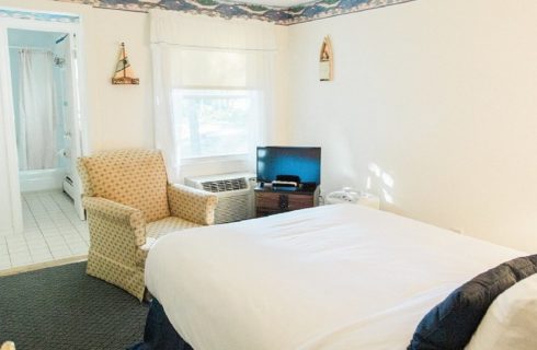 Bedroom with yellow sitting chair, single bed, TV and doorway into tiled bathroom