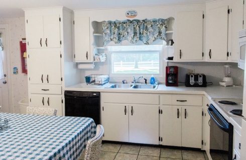 Kitchen with white counters and cabinets, window and table with blue checkered tablecloth