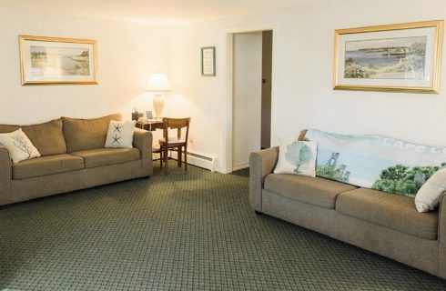 Living room of a cottage with two tan couches, small desk and framed artwork on the walls