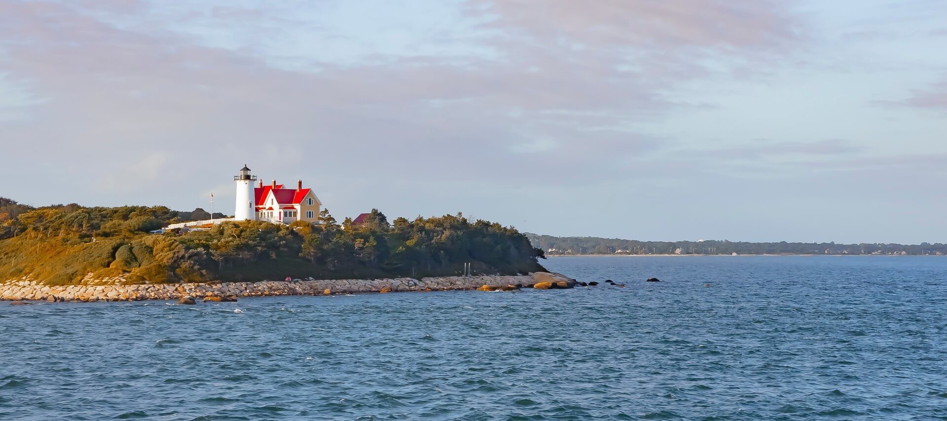 A white and red lighthouse on a peninsula surrounded by water and cloudy skies