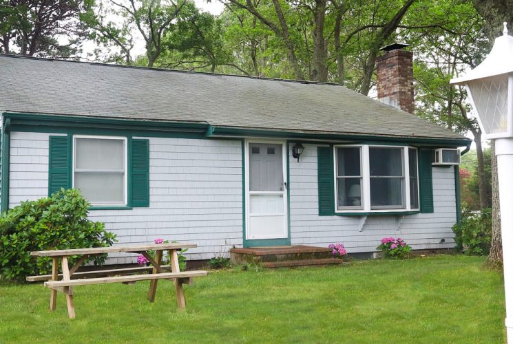 Front facade of a cottage with grey siding and green shutters and white lamppost