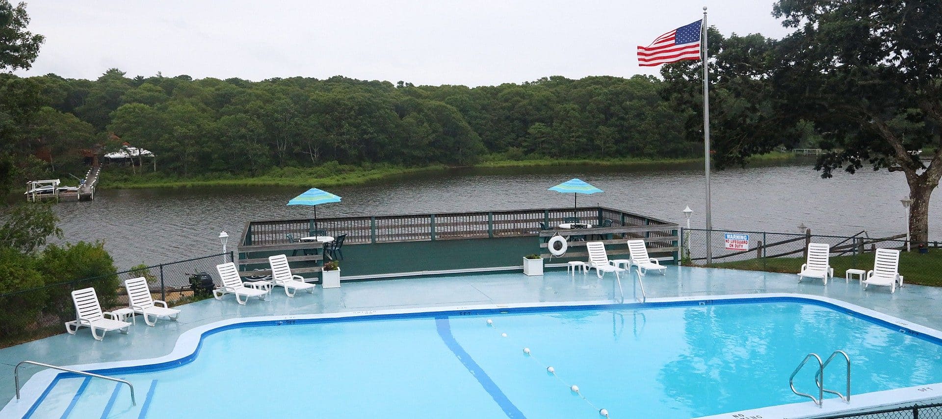 Large pool with white lounging chairs and overlook deck next to a large waterway