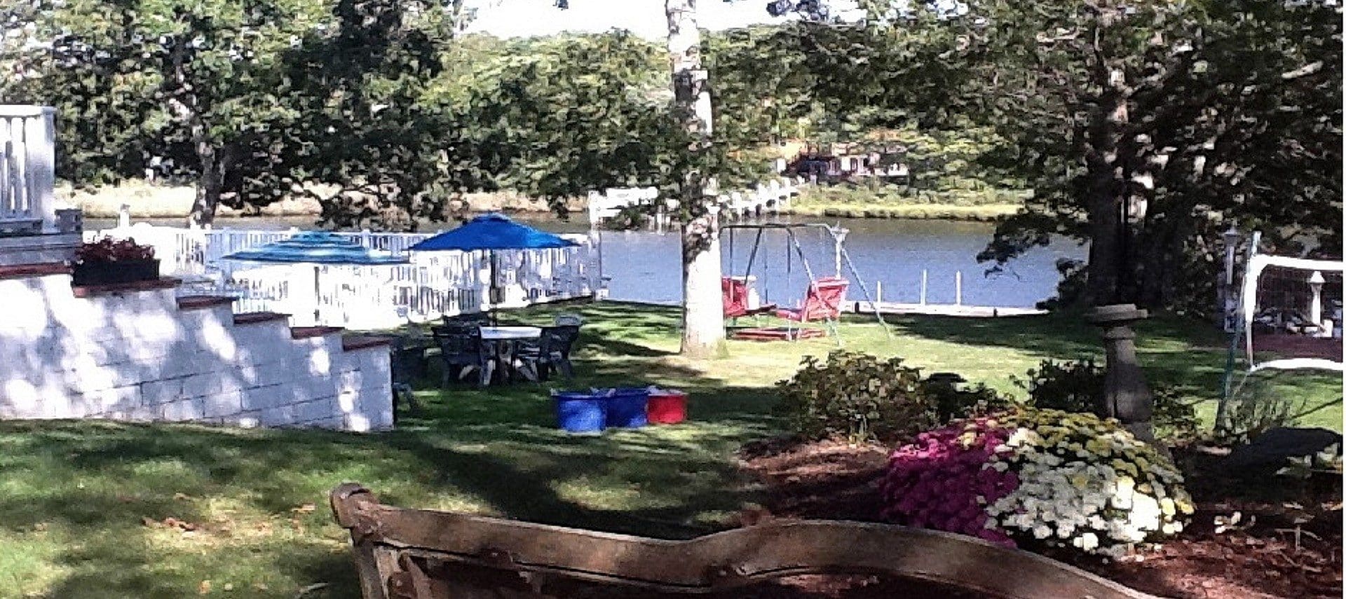 Outdoor garden area with green lawn, flowers, patio tables and benches all next to a riverway