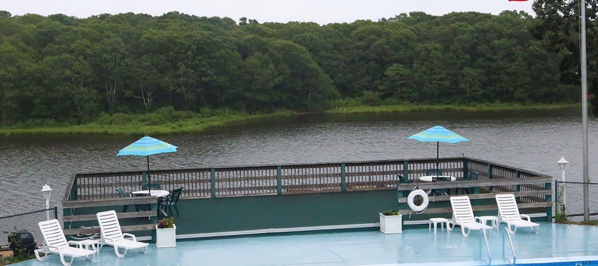 Several white lounging chairs near a large deck overlooking a body of water