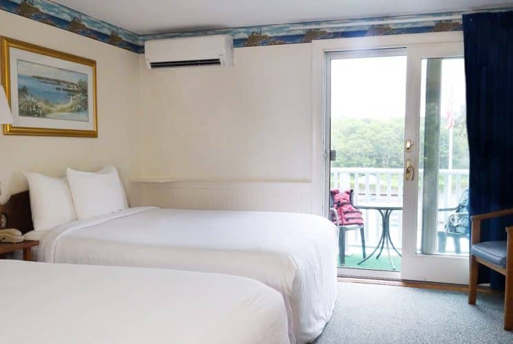 Guest room with two beds in white linens, sitting chair and patio slider leading to an outside deck